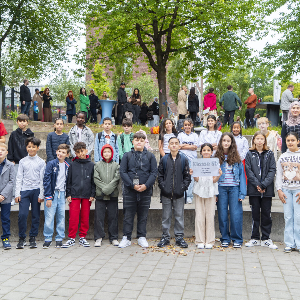 Die neue Klasse 5b steht gemeinsam mit ihrem Klassenteam für ein Gruppenfoto auf dem Schulgelände.