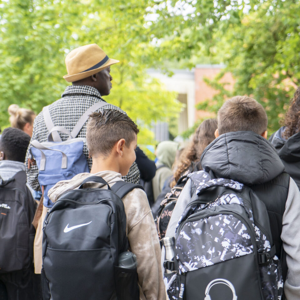 Zwei neue Fünftklässler mit großen Schulrucksäcken stehen während der Einschulungsfeier in einer Gruppe von Schüler:innen.