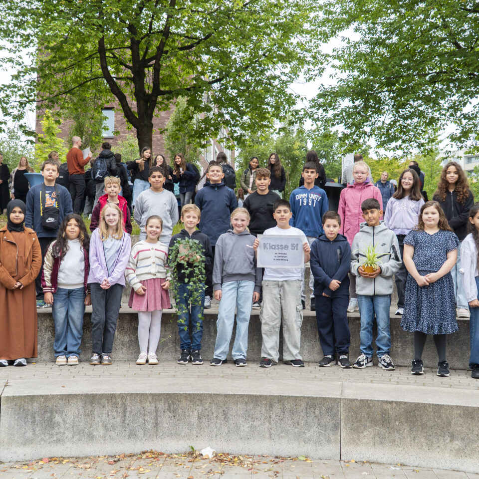 Die neue Klasse 5f steht gemeinsam mit ihrem Klassenteam für ein Gruppenfoto auf dem Schulgelände.