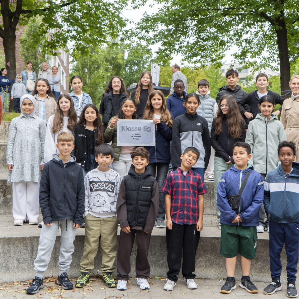 Die neue Klasse 5g steht gemeinsam mit ihrem Klassenteam für ein Gruppenfoto auf dem Schulgelände.