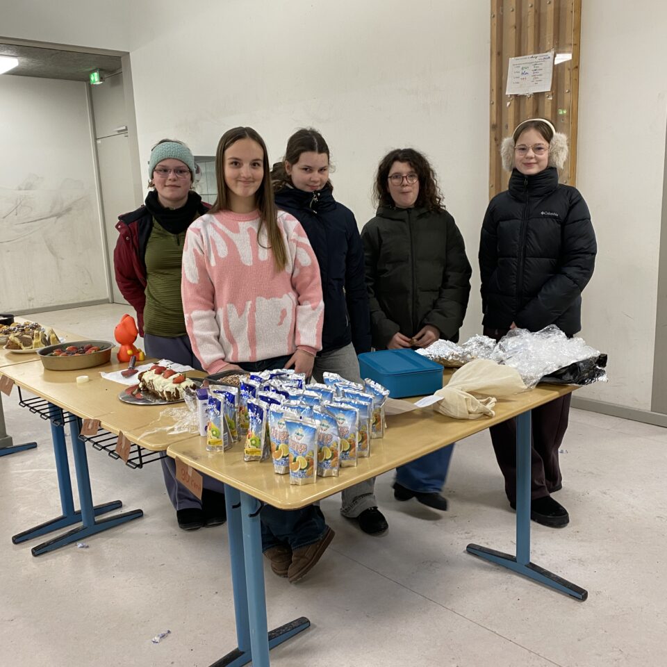 Fünf Schüler:innen der Klasse 7b stehen hinter ihrem Verkaufsstand mit Kuchen und Getränken für die Spendenaktion zugunsten des Kinderkrankenhauses Harburg.