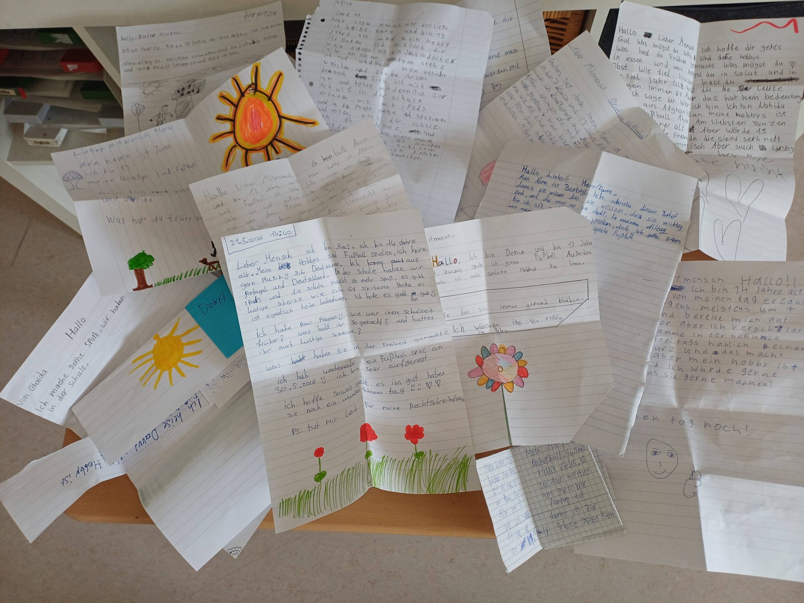 Handgeschriebene Briefe der Klasse 7f an Bewohner:innen eines Pflegeheims liegen ausgebreitet auf einem Tisch. Viele sind mit bunten Sonnen, Blumen und Herzen verziert.